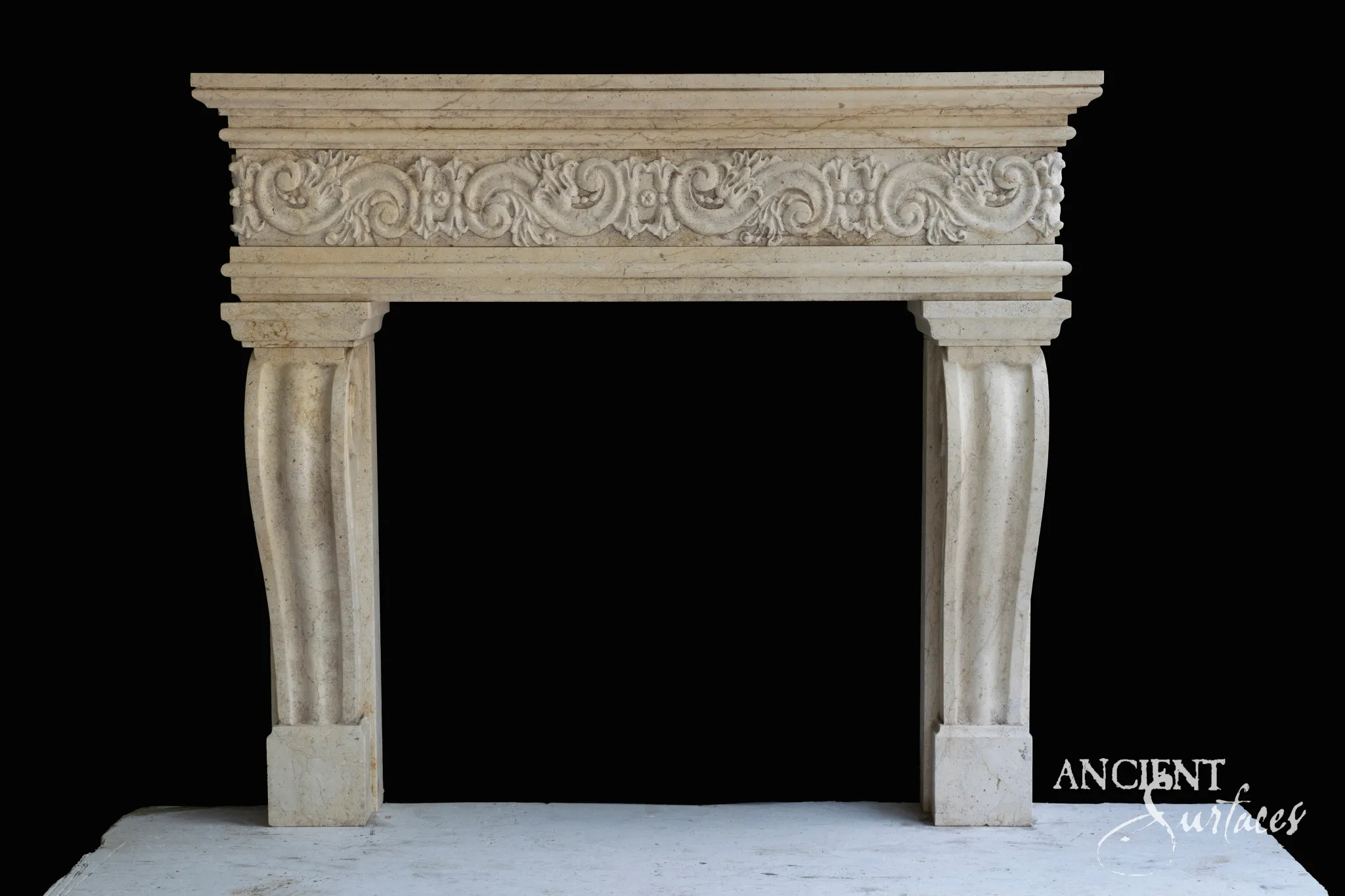 Reclaimed antique limestone mantel from Ancient Surfaces on a black ground, with a plain moulded shelf, a frieze of continuous carved scrollwork and small flowers, and smooth curved legs hollowed by a single broad flute