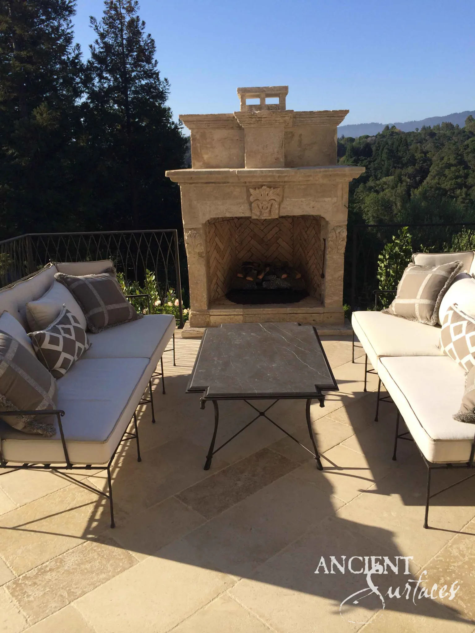 Reclaimed antique limestone mantel from Ancient Surfaces built as an outdoor fireplace on a hilltop terrace, with a moulded cornice shelf, a carved foliate keystone and a stepped chimney breast above a herringbone firebox
