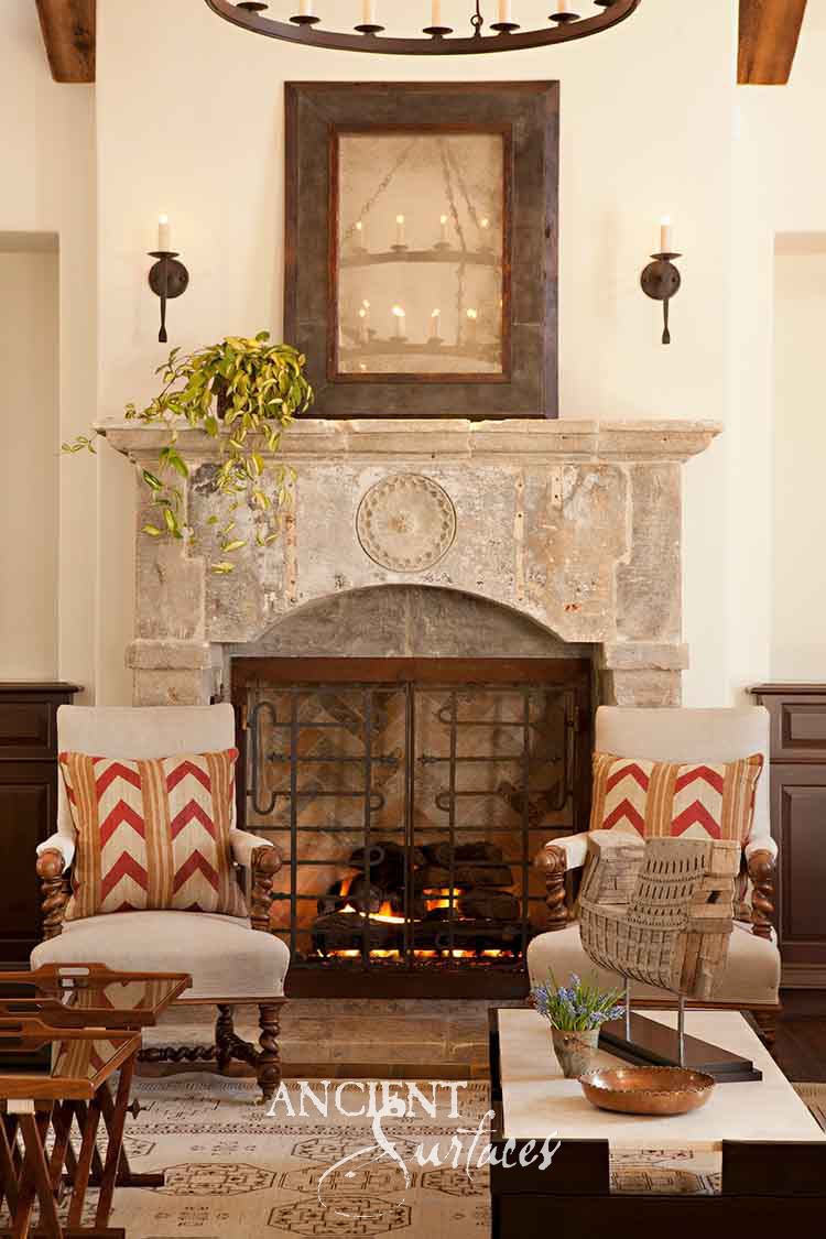 Reclaimed antique limestone mantel from Ancient Surfaces with a jointed built up shelf, one carved rosette medallion on the frieze and a segmental arched opening closed by iron fire doors