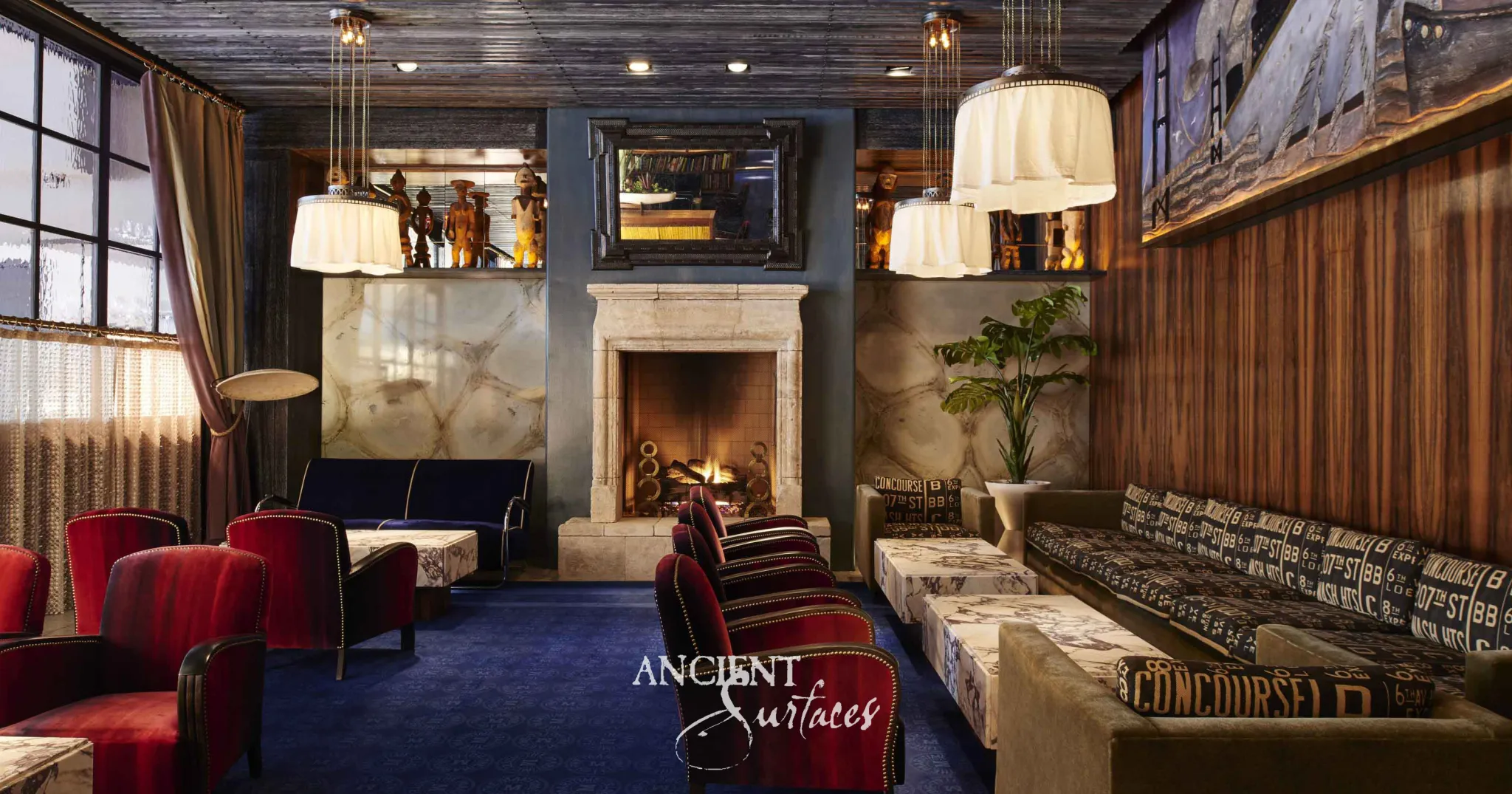 Reclaimed antique limestone mantel from Ancient Surfaces with a plain moulded shelf and undecorated frieze, its arched firebox lit in a dark panelled lounge