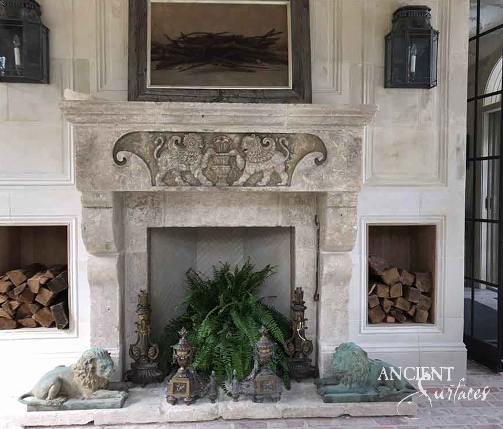 Reclaimed antique limestone mantel from Ancient Surfaces carved with two facing lions flanking an urn on a sunken frieze panel, under a heavy worn shelf, with corbelled jambs and a herringbone firebox