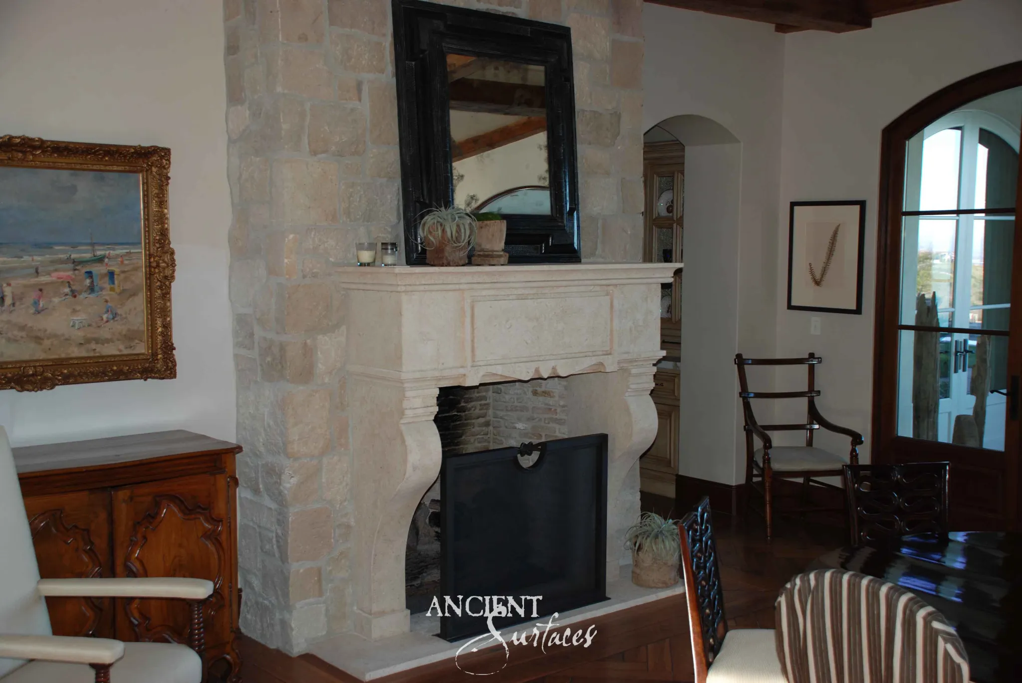 Reclaimed antique limestone mantel from Ancient Surfaces against a rubble stone chimney breast, with a thick rounded shelf, a panelled frieze finishing in a scalloped apron and heavy curved console legs