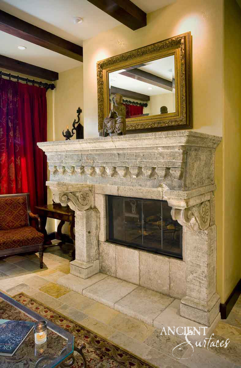 Reclaimed antique limestone mantel from Ancient Surfaces in weathered grey stone, its frieze carved as a row of heavy pendant drops under a deep shelf, with rosette carved corbels above plain jambs