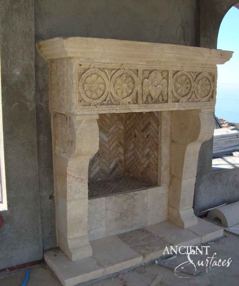 Reclaimed antique limestone mantel from Ancient Surfaces standing on a terrace by the sea, its frieze carved with two rosette roundels flanking a panel of facing winged figures, above scrolled legs and a herringbone recess